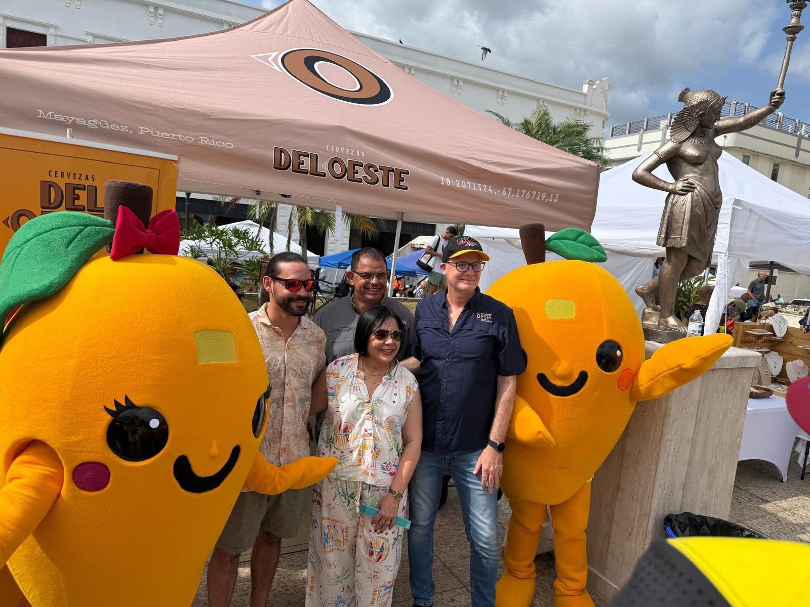 Grupo posando con las mascotas del festival frente al booth de Cervezas del Oeste