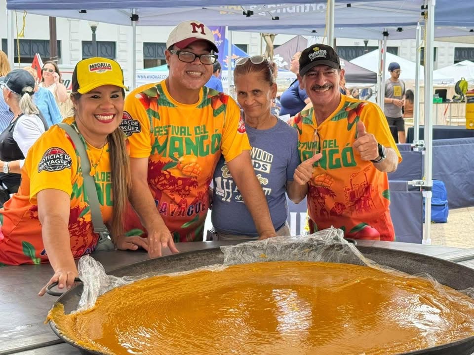 Equipo del Festival del Mango con la camisa anaranjada oficial frente a la paellera gigante